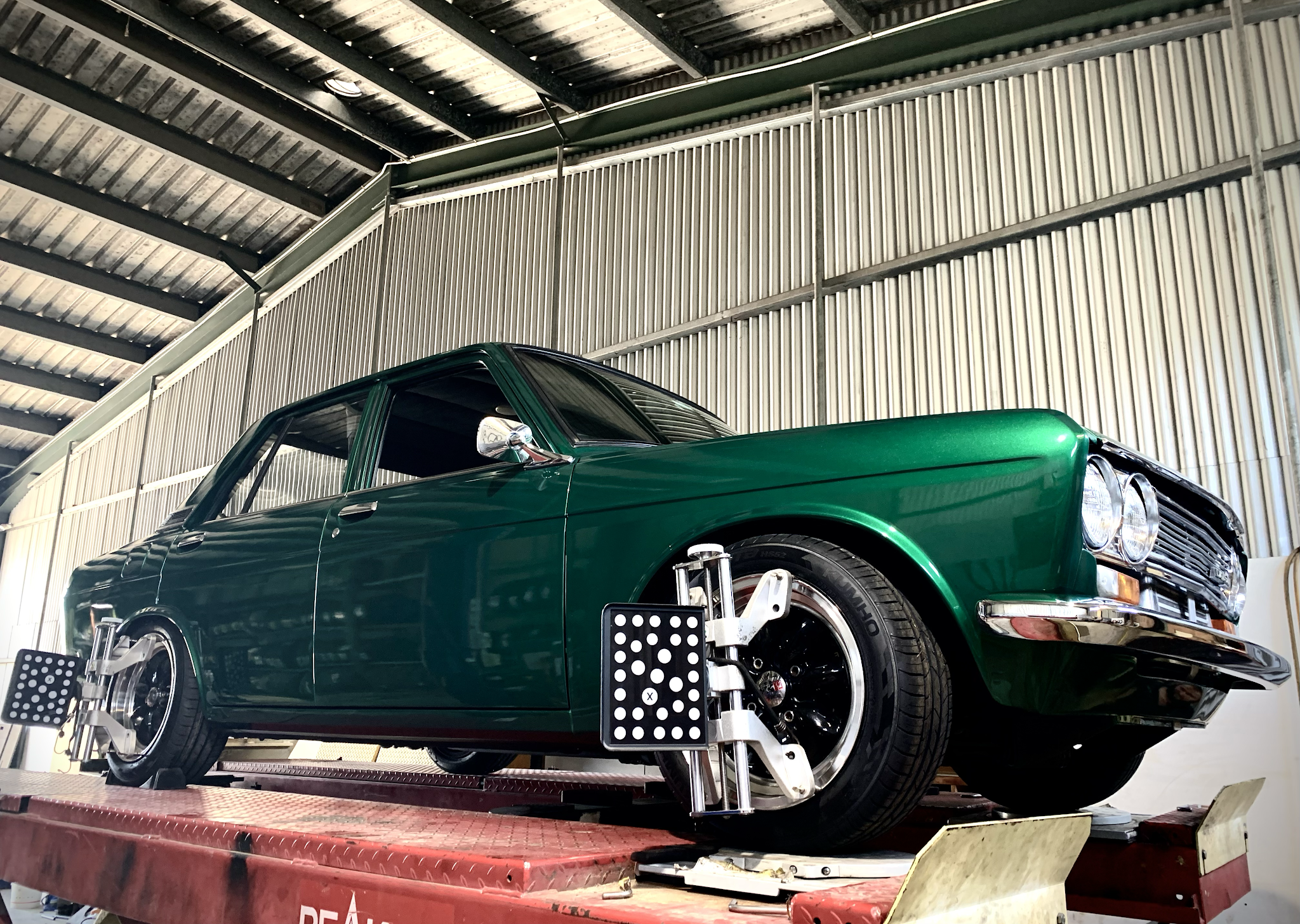 A dark green Datsun on the alignment rack with camera targets clamped to the wheels
